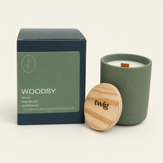 Green candle with wooden lid and packaging labeled 'Woodsy' on a beige background