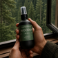 Person holding a bottle of 'Woodsy' product with a forest view in the background