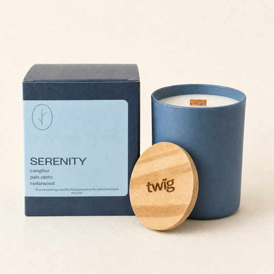 Blue candle with wooden lid and 'twig' branding next to a 'Serenity' box on a beige background