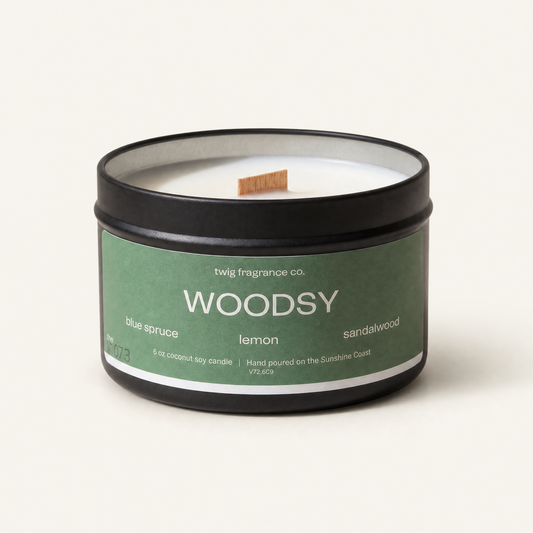 Candle in a tin labeled 'Woodsy' by twig fragrance co. on a white background