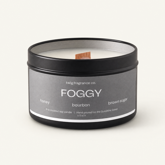 Candle in a black tin labeled 'Foggy' with a gray label on a white background